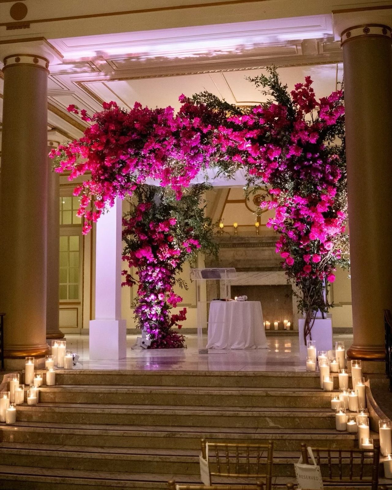 A ceremony arch of magenta blooms above candlelit stairs